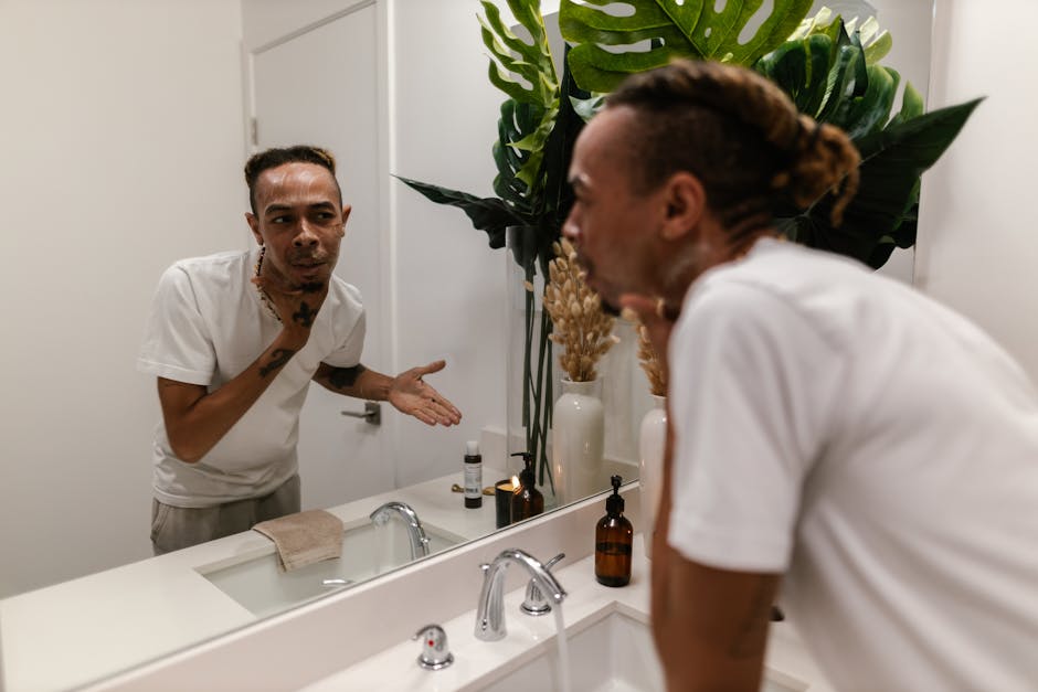 A young man applying skincare product while looking in the mirror in a modern bathroom