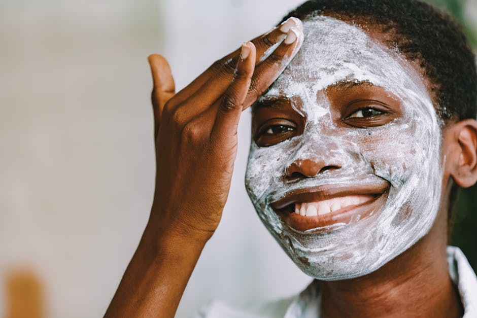A black woman joyfully applying skincare cream to her face indoors