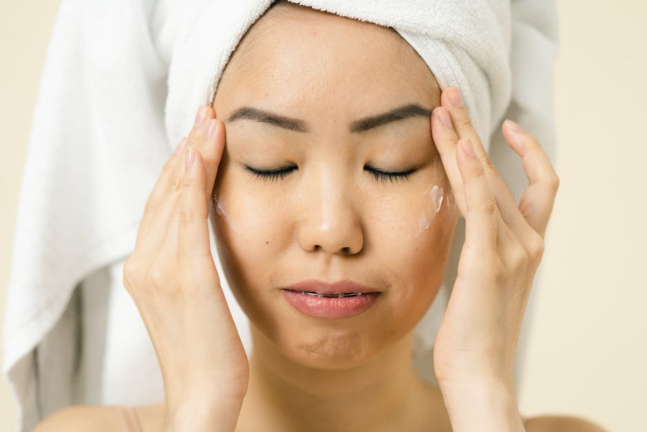Asian woman with a towel on head applying moisturizer for skincare routine