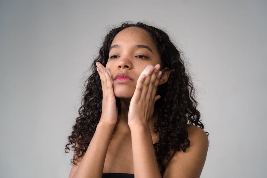 A young woman with curly hair gently applies skincare cream to her face