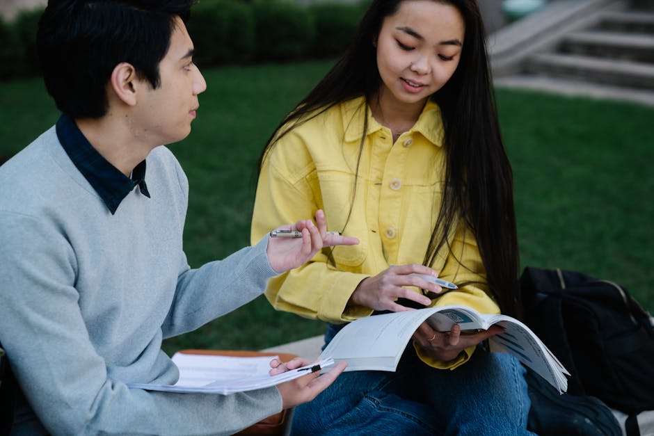 Two students engage in outdoor study session with textbooks and notes.